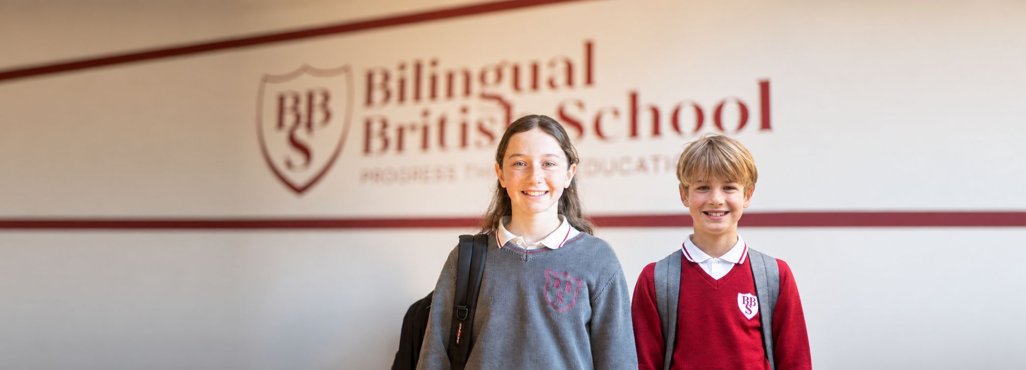 Due studenti BBS sorridenti in divisa davanti all’insegna Bilingual British School